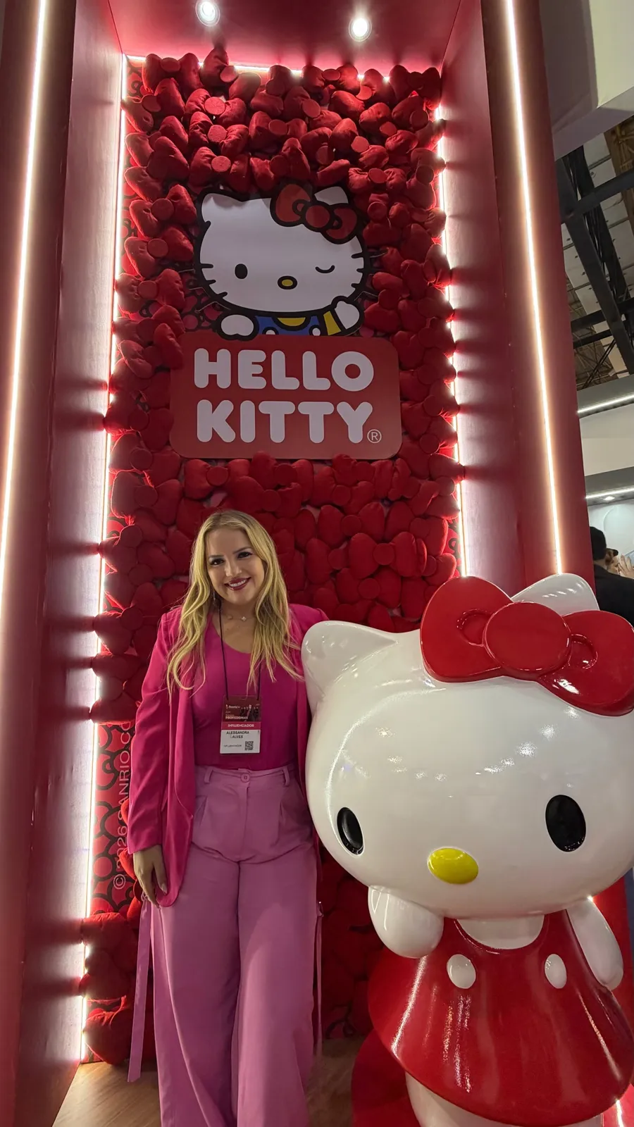 Alessandra ao lado de uma estátua da Hello Kitty em parede de rosas vermelhas