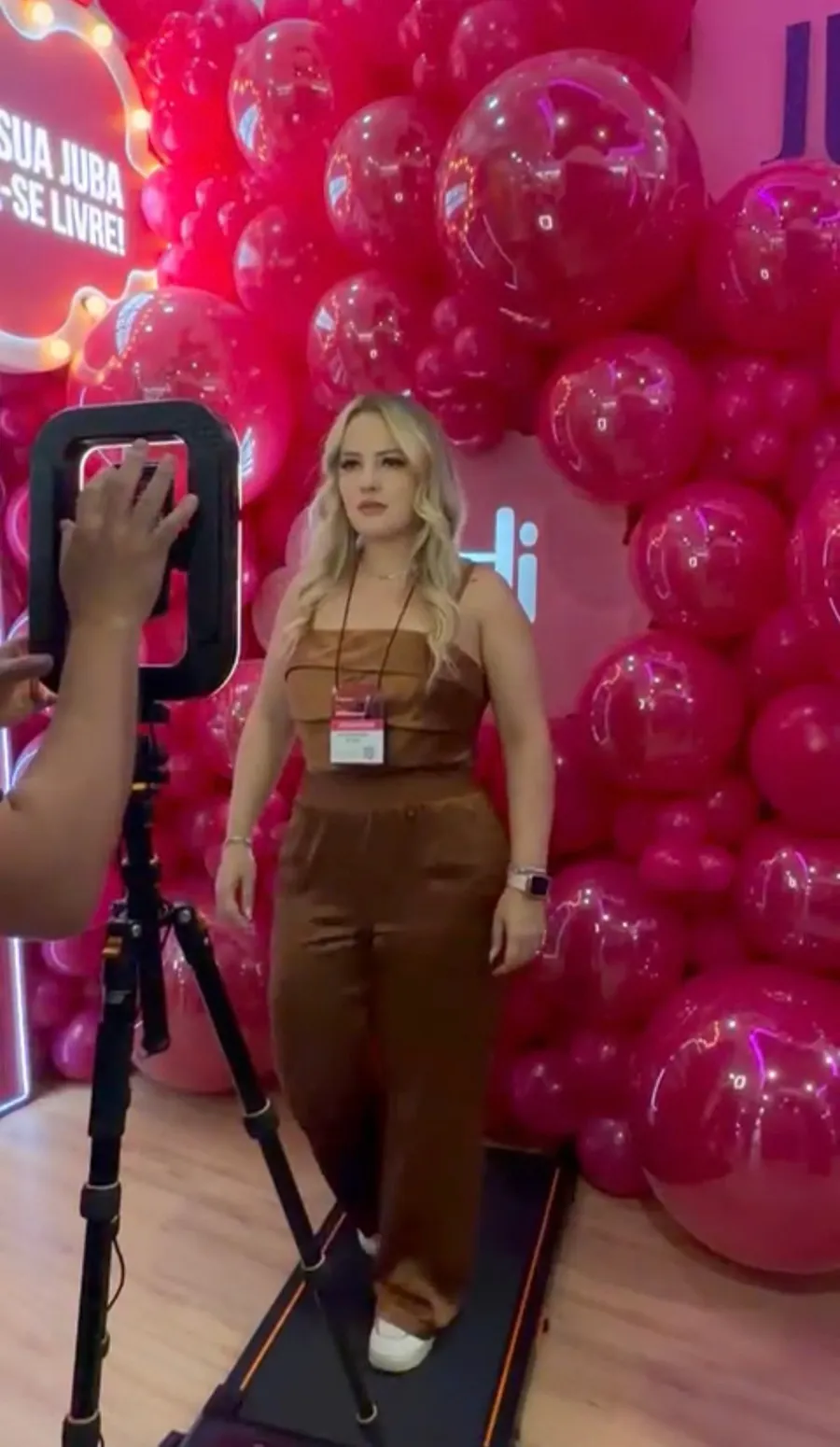 Alessandra gravando conteúdo diante de painel de balões rosa